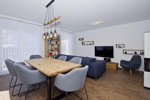 A modern living room with a wooden dining table, grey upholstered chairs, a blue sofa, a bookshelf, a flat-screen TV, and a fireplace. - Vacation home Luna - Holiday home Luna semi-detached house (Breege)