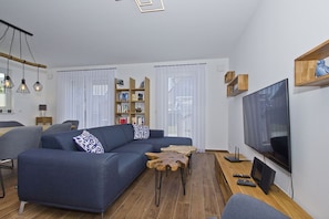 Un salon moderne avec un canapé d’angle, une table basse en bois, un téléviseur et une bibliothèque.
