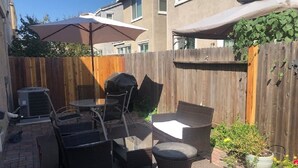 Un espace extérieur aménagé en terrasse, avec une table et des chaises, une petite table ronde et une poubelle.