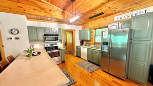 Une cuisine avec des meubles de rangement en bois, un four à micro-ondes, une cuisinière, un réfrigérateur et une horloge au mur.