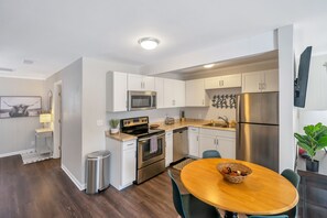 Una cocina moderna con armarios blancos, electrodomésticos de acero inoxidable y una mesa de comedor de madera.