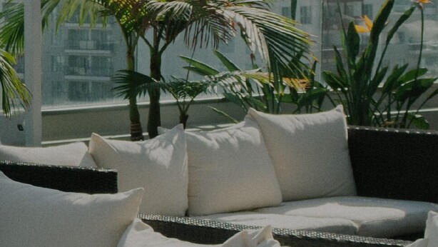 A balcony with a sofa, white cushions, and potted plants.