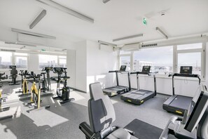 A modern gym with various exercise machines, large windows, and a city view.