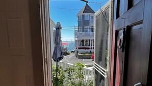 A view through a door to a balcony with a wooden floor, a white picket fence, and a red door.