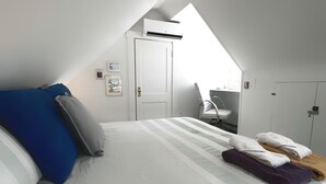 A bedroom with a sloped ceiling, a bed with striped bedding, a chair, and a wardrobe.