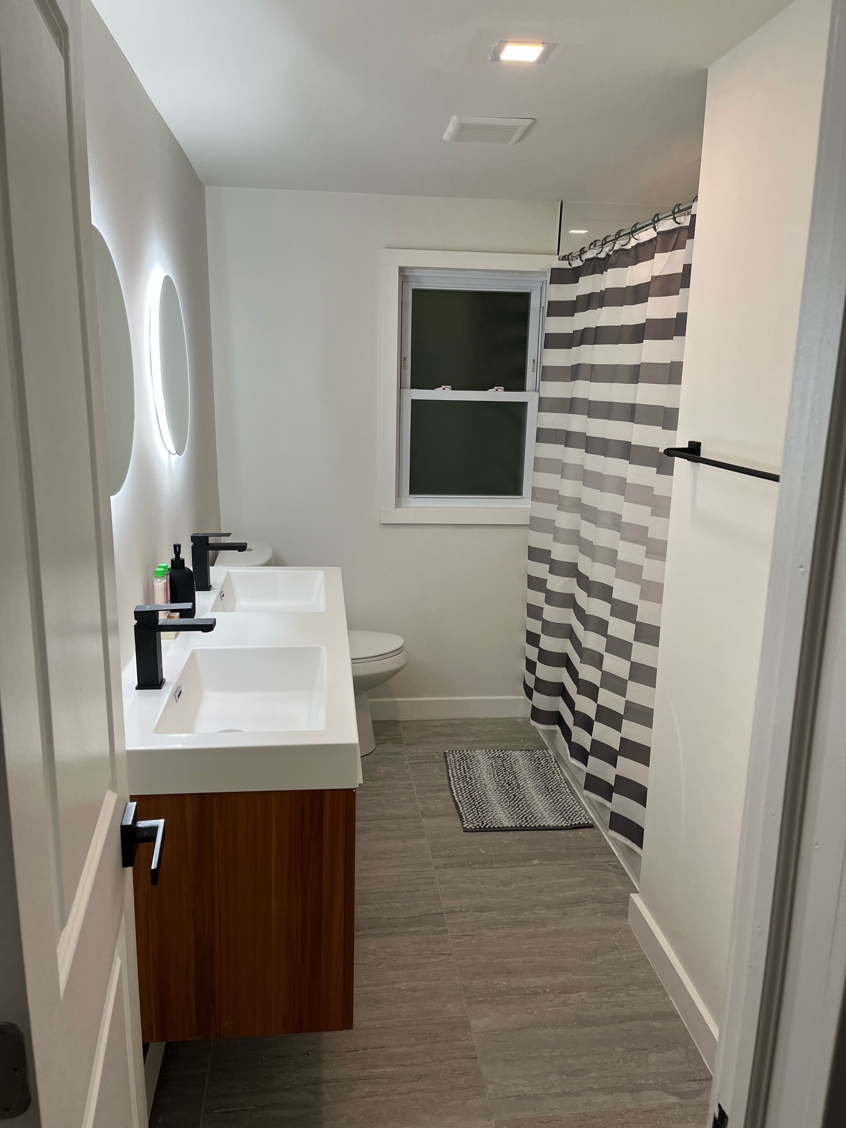 A modern bathroom with two sinks, a toilet, and a window.