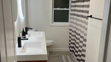 A modern bathroom with two sinks, a toilet, and a window.