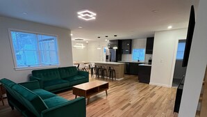Amplia sala de estar con un sofá verde, una mesa de centro de madera y una cocina al fondo.