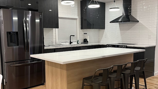 Una cocina moderna con un refrigerador de acero inoxidable, una isla grande con taburetes de bar e iluminación colgante.