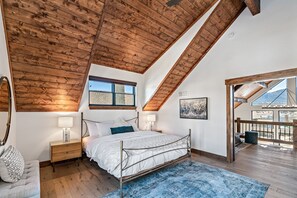 A bedroom with a sloped ceiling, a large window, a bed, bedside tables, and a view of the outside. - Indoor/Outdoor Fireplace, Jacuzzi, Heated Bathroom Floors (Estes Park)