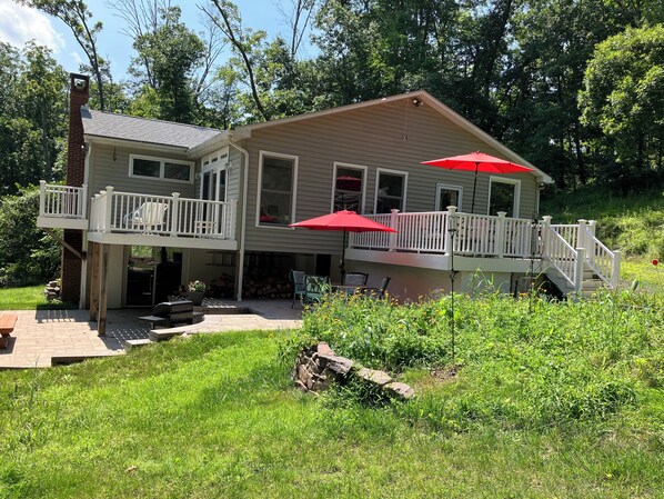 A two-story house with a balcony, a covered patio, and a red umbrella. - Creekside Retreat-spacious cottage nestled in the wildflowers and lush woods (Harleysville)