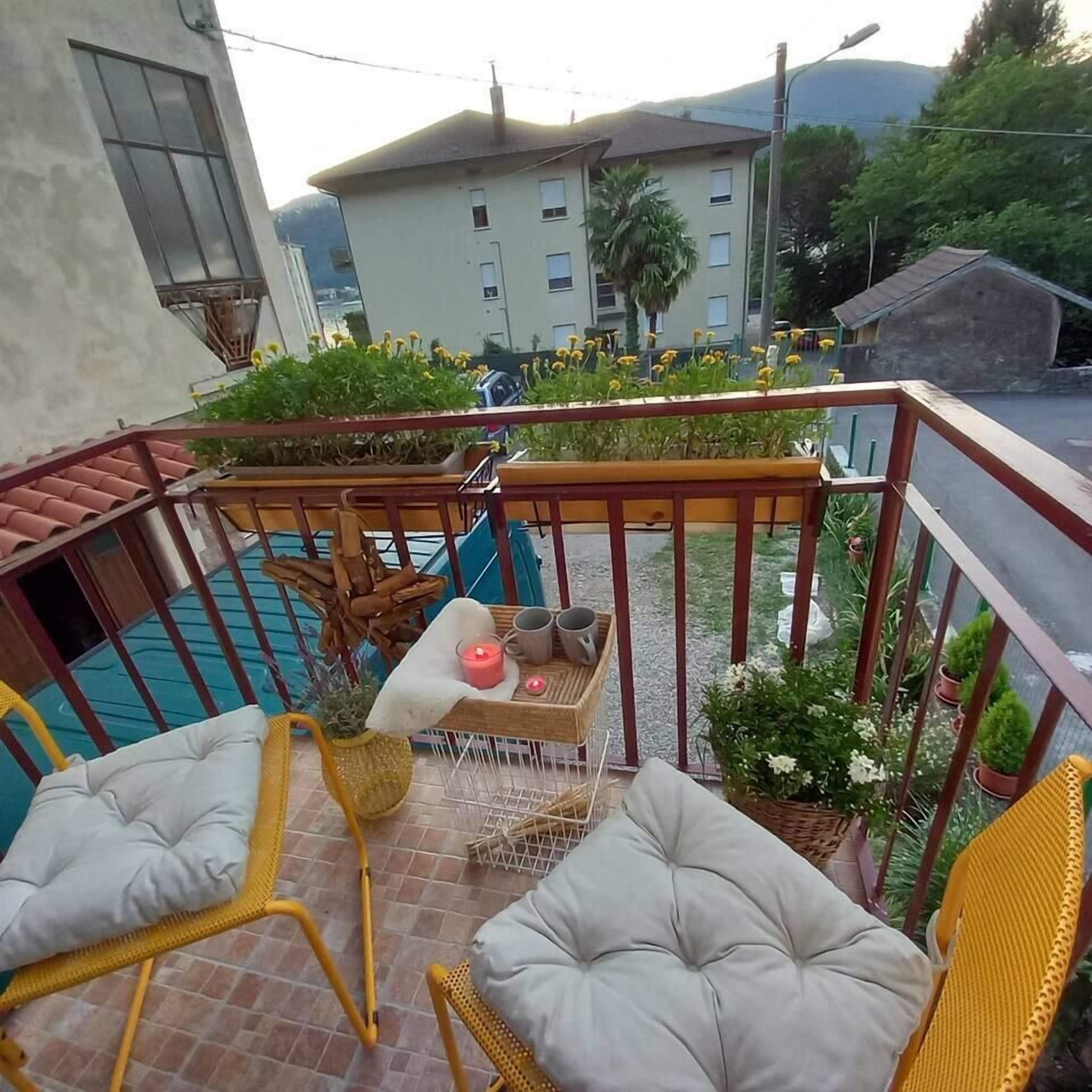 Ein Balkon mit gelben Korbstühlen, einem kleinen Tisch mit Kerze und Topfpflanzen.
