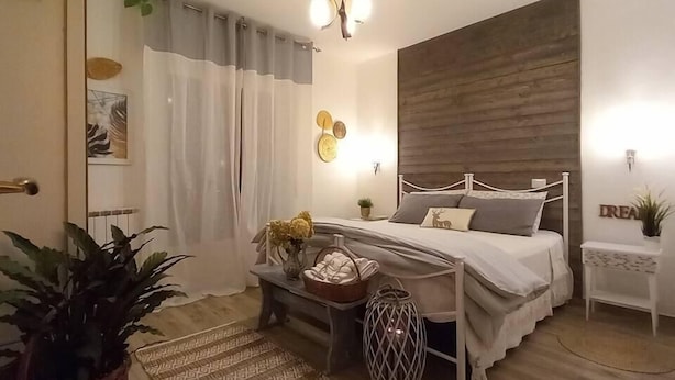 Un dormitorio con cama, mesita de noche, lámpara, reloj de pared y una planta en la mesita.
