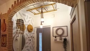 Un pasillo con un arco de ladrillo, un espejo, una puerta con panel de vidrio esmerilado y una lámpara colgante.