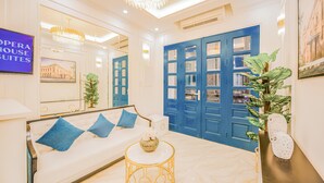A hotel room with a white sofa, a round gold side table, and a large mirror. There is a blue door and a chandelier. - Opera House Suites (Hanoi)