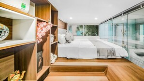 A modern bedroom with a large bed, a wooden vanity, and a glass shower enclosure. - Opera House Suites (Hanoi)