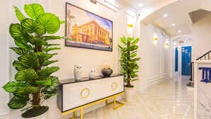 A hallway with a white console table, two potted plants, a framed picture on the wall, and a blue door in the background. - Opera House Suites (Hanoi)