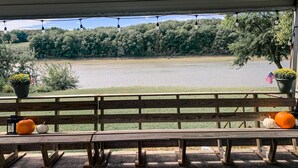 A wooden bench with potted plants and pumpkins, overlooking a lake with trees and a grassy area. - Des Moines River Front Cabin- Fishing/Hunting/Kayaking (Keosauqua)