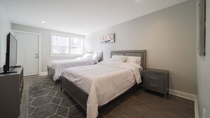 Un dormitorio con dos camas, un aparador, un televisor y una ventana con persianas.
