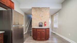 Una cocina con refrigerador de acero inoxidable, armarios de madera, pared de ladrillo y encimera de granito.