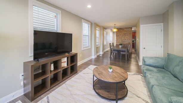 Una sala de estar con televisor, mueble de madera para equipo audiovisual, una mesa de centro redonda y un sofá verde.