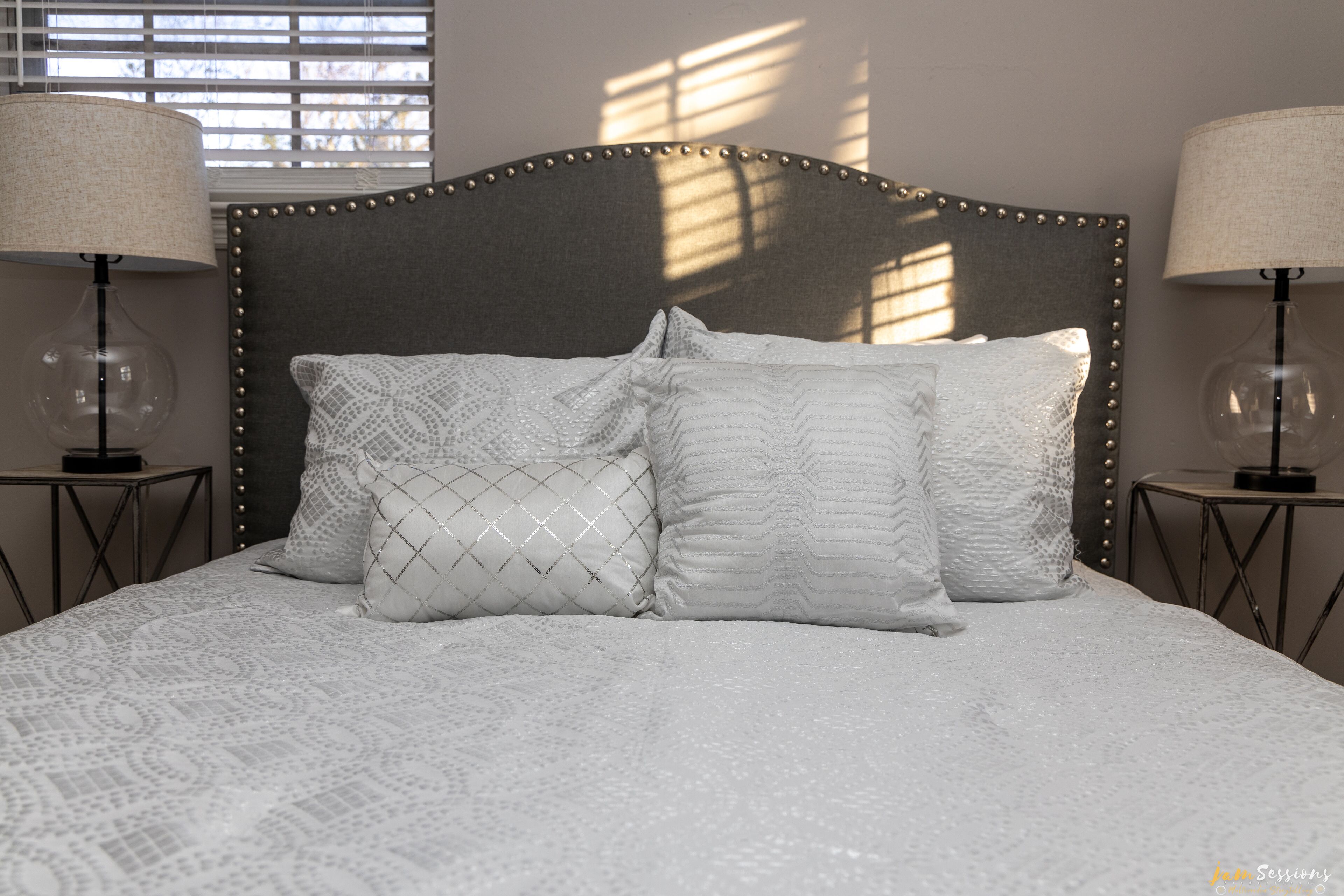 Un lit bien fait, recouvert d’une couvre-lit à motifs et agrémenté de trois oreillers, avec deux lampes de chaque côté.