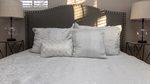 Cama bem arrumada com colcha estampada e três almofadas, com duas luminárias de cada lado.