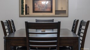 A dining table with six chairs, a chandelier, and a framed picture on the wall.
