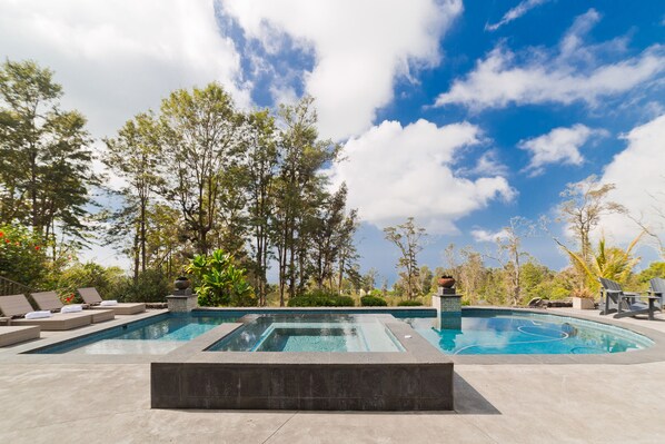 Une piscine rectangulaire bordée de pierres, entourée de chaises longues et offrant une vue sur les arbres et le ciel.