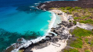 Vue aérienne d’une zone côtière avec une plage, un littoral rocheux et des eaux d’un bleu limpide.
