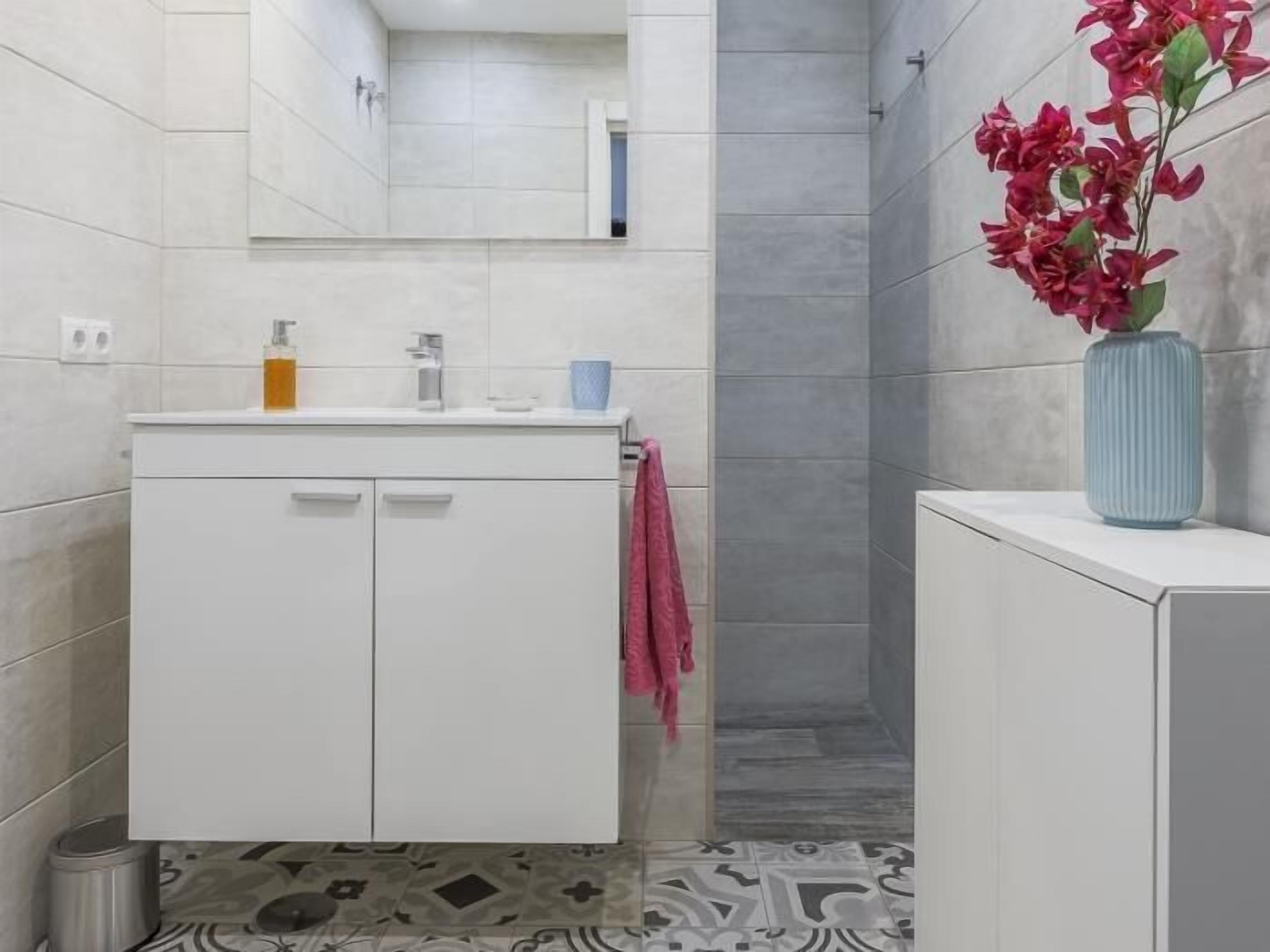 A bathroom with a white vanity, a mirror, and a vase with flowers.