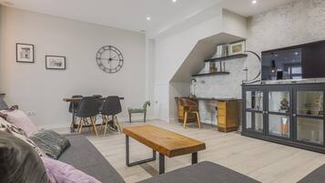 A modern living room with a sofa, a wooden coffee table, and a dining area with chairs and a small table.