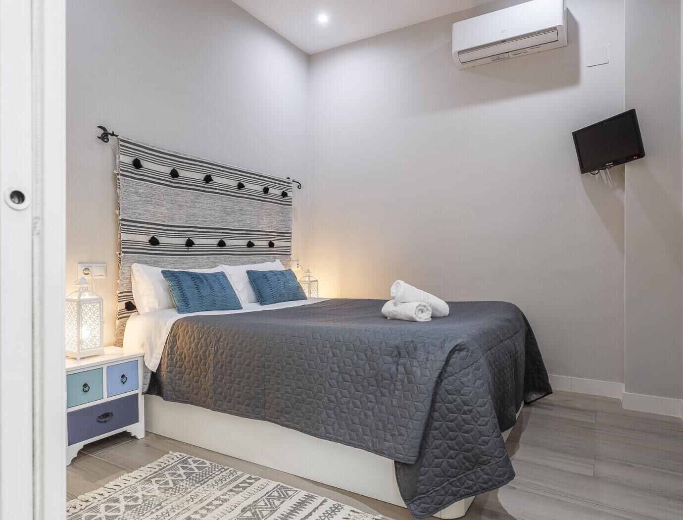 Un dormitorio con cama, mesitas de noche, lámpara y televisor.