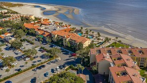 Luftaufnahme eines Küstenhotels mit mehreren Gebäuden, einem Parkplatz und einem Strand.