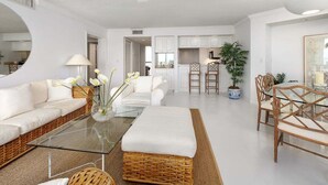 Ein modernes Wohnzimmer mit einem Glastisch, weißen Sofas, Korbmöbeln und einem Essbereich mit Holzsesseln.