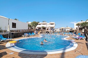 A swimming pool with lounge chairs and umbrellas, surrounded by buildings with balconies. - Apartment 'Flamingo 62' with Private Terrace & Shared Pool (Playa Blanca)