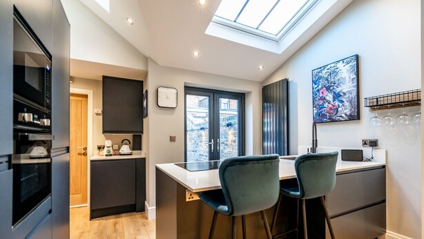 A modern kitchen with a skylight, a dining area with two bar stools, and a view of the city through large windows.