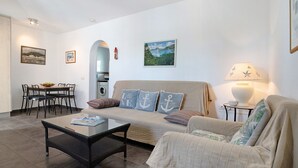 A living room with a sofa, a coffee table, a dining table with chairs, a lamp, and artwork on the walls. - Apartment 'Jardin del Sol 26' with Terrace, Shared Pool& Wi-Fi (Playa Blanca)