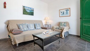 A room with a sofa, a glass-top table, a green door, and two framed pictures on the wall. - Apartment 'Jardin del Sol 26' with Terrace, Shared Pool& Wi-Fi (Playa Blanca)