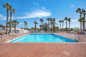 Une piscine rectangulaire à l’eau d’un bleu cristallin, entourée de palmiers et bordée d’une terrasse carrelée.