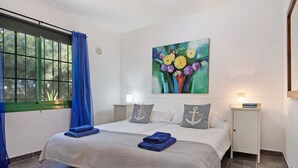 A bedroom with a large bed, a nightstand, a painting, and a window with curtains. - Apartment 'Jardin del Sol 26' with Terrace, Shared Pool& Wi-Fi (Playa Blanca)
