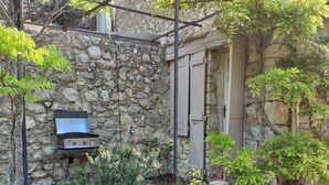 A stone building with a grill and a door, surrounded by greenery and a gravel path. - Charming renovated sheepfold in a natural setting, not overlooked, private swimming pool (La penne sur l'ouveze)