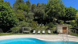 A swimming pool with clear blue water, surrounded by lounge chairs and a small building, likely a changing room or storage, set against a backdrop of lush trees. - Charming renovated sheepfold in a natural setting, not overlooked, private swimming pool (La penne sur l'ouveze)