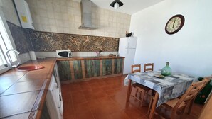 A kitchen with a tiled backsplash, a microwave, a sink, a dining table with chairs, and a wall clock.
