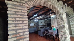 An interior with a brick archway, a stone wall, a fireplace, and a dining area with chairs and a table.