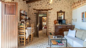 A rustic room with a stone wall, wooden furniture, a television, and a bookshelf. - Country Home "Can Pulit" with Pool, Garden, A/C & Wi-Fi (Selva)