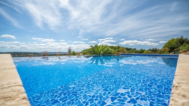 A clear blue swimming pool with a tiled bottom, surrounded by a stone deck, with a view of trees and hills in the background. - Country Home "Can Pulit" with Pool, Garden, A/C & Wi-Fi (Selva)
