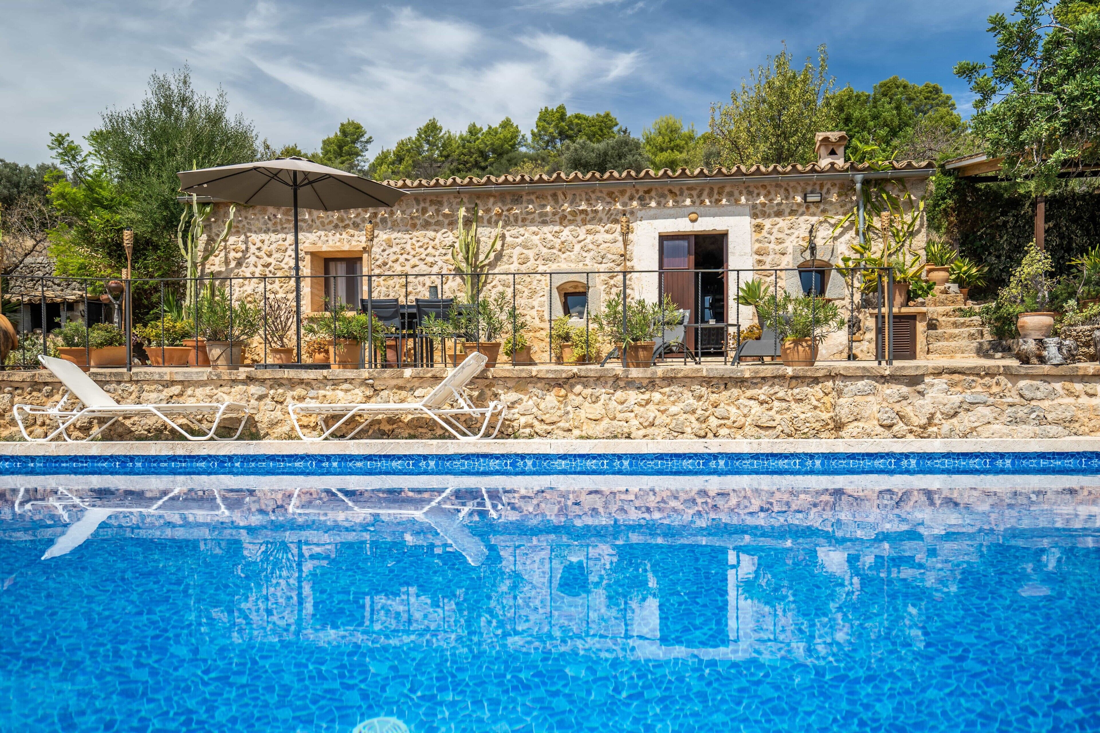 A stone building with a pool, outdoor seating, and potted plants.