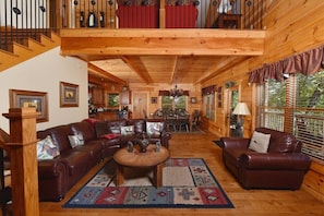 A spacious wooden cabin with a living area featuring a large leather sofa, a coffee table, and a dining area with a chandelier.