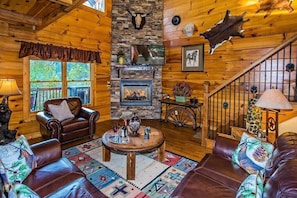 A rustic cabin interior with a stone fireplace, leather furniture, and wooden walls.